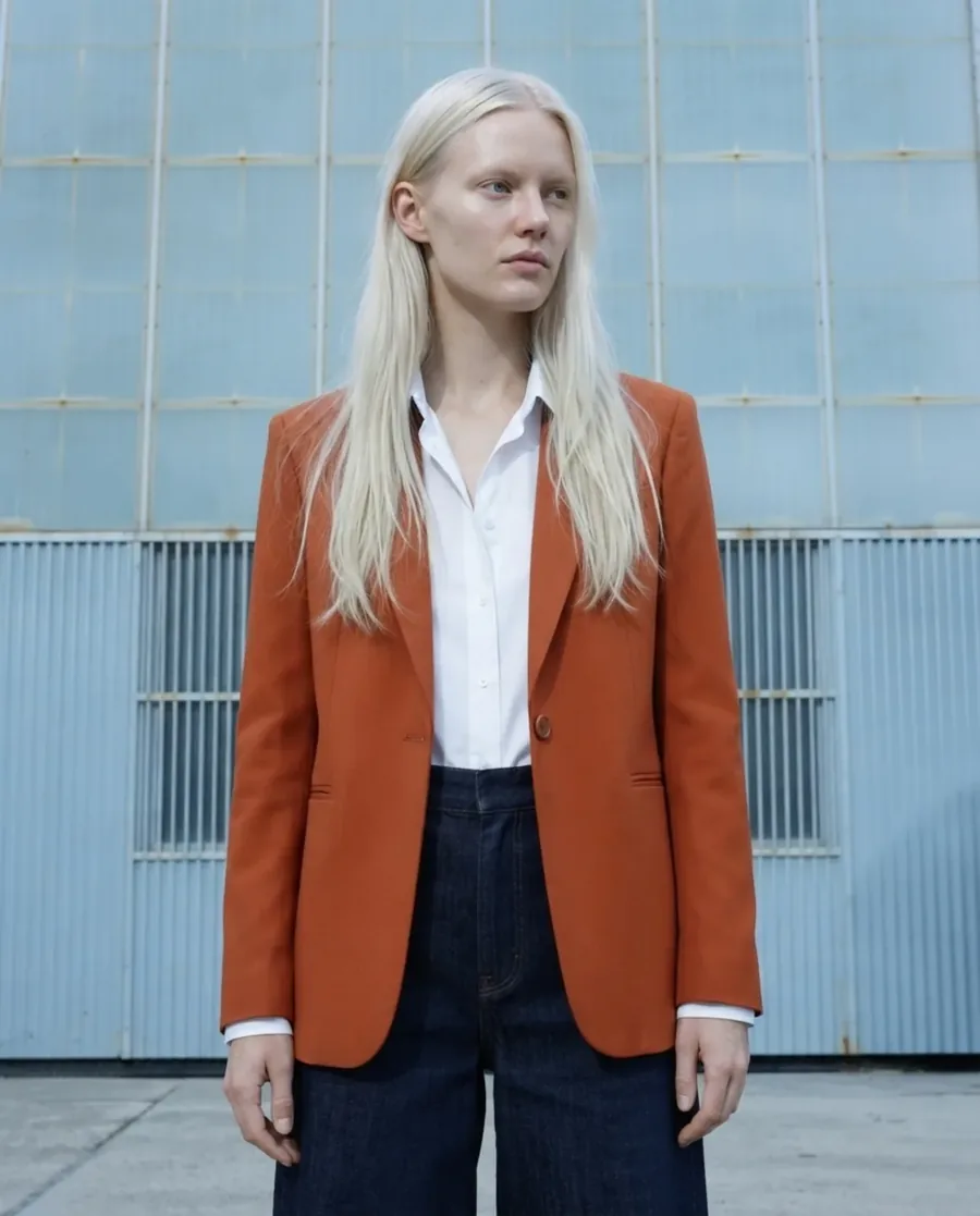 Rust blazer and navy trousers on an AI model against a blue tiled wall